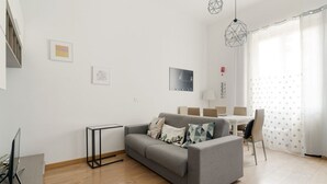 Een moderne woonkamer met een grijze bank, een kleine tafel en een eethoek met stoelen.