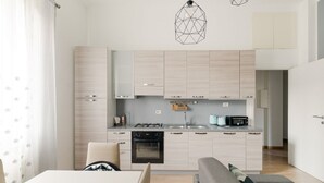 Een moderne keuken met lichte houten kastjes, een ingebouwde oven en een eethoek met een tafel en stoelen.