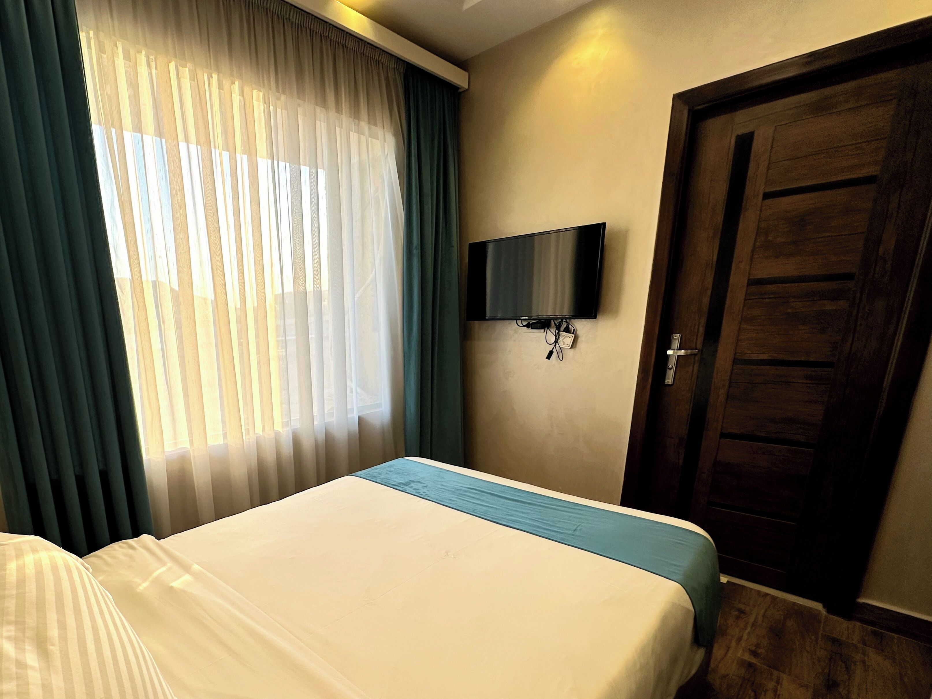 Une chambre d’hôtel avec un lit, un téléviseur fixé au mur et une porte.