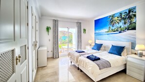 A hotel room with two beds, a large beach mural, a sliding glass door to the balcony, and a white wardrobe.