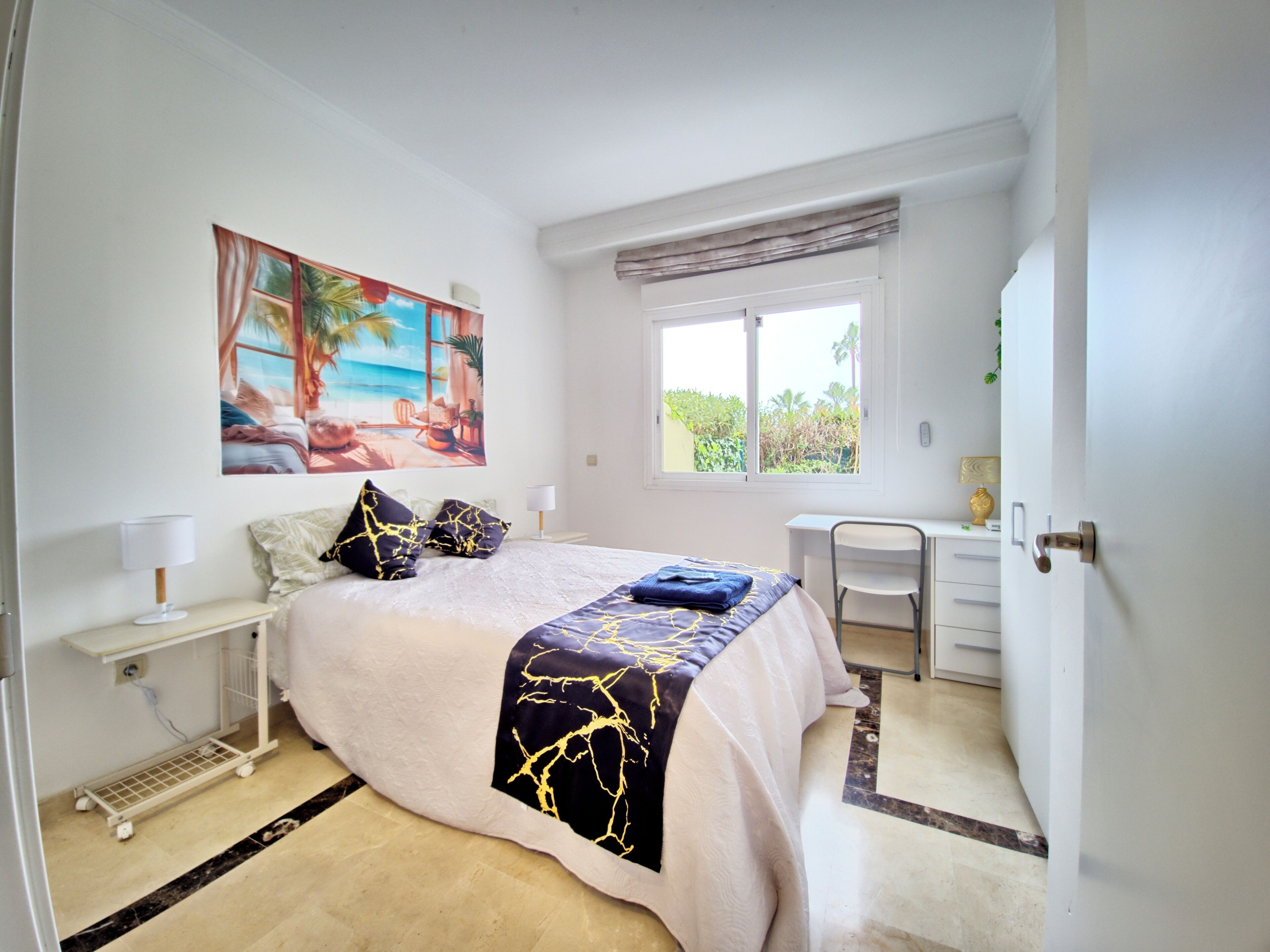 Una camera da letto con un letto, una scrivania, una sedia, una finestra e un quadro appeso al muro.