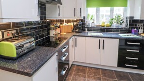 A modern kitchen with black and white cabinetry, a granite countertop, and a window with a green blind. - Marwood (Penrith)