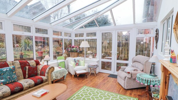 A conservatory with a glass roof, wooden flooring, and a variety of seating including a sofa, chairs, and a table. - Marwood (Penrith)