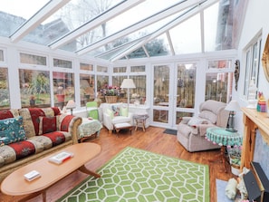 A conservatory with a glass roof, wooden flooring, and a variety of seating including a sofa, chairs, and a table. - Marwood (Penrith)
