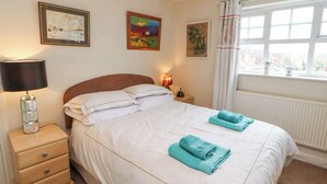 A bedroom with a bed, a nightstand, a lamp, and a window with curtains. - Marwood (Penrith)