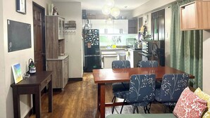 A compact living space with a dining area, kitchenette, and a small seating area with patterned chairs. - Spacious 3BR Senja Pasig Home - Sleeps Up To 9! (Pasig)