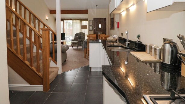 Una cocina moderna con encimera de granito negro, electrodomésticos de acero inoxidable y una escalera de madera que sube a una sala de estar.