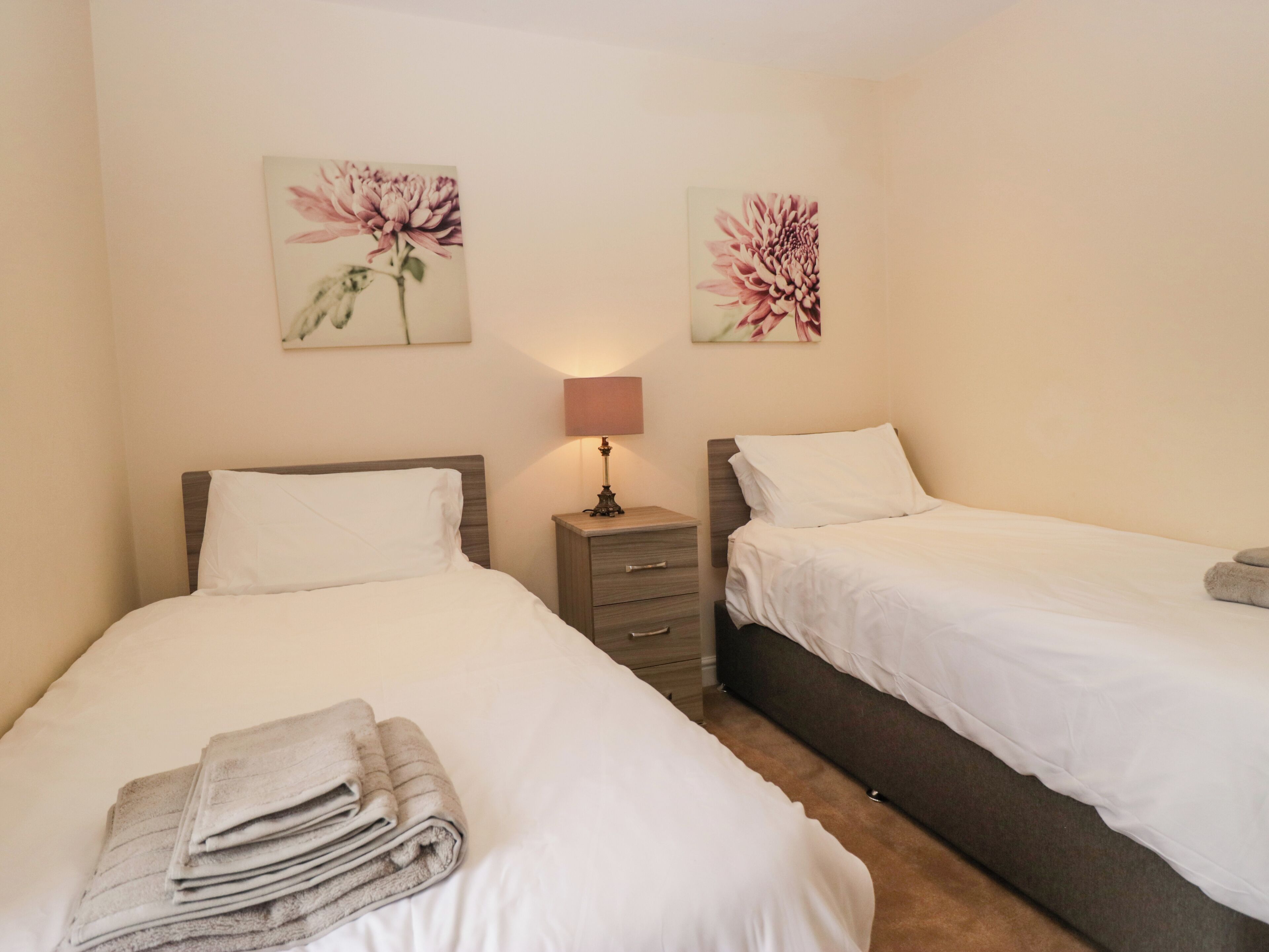 Ein Hotelzimmer mit zwei Betten, einem Nachttisch mit Lampe und floralen Bildern an den Wänden.