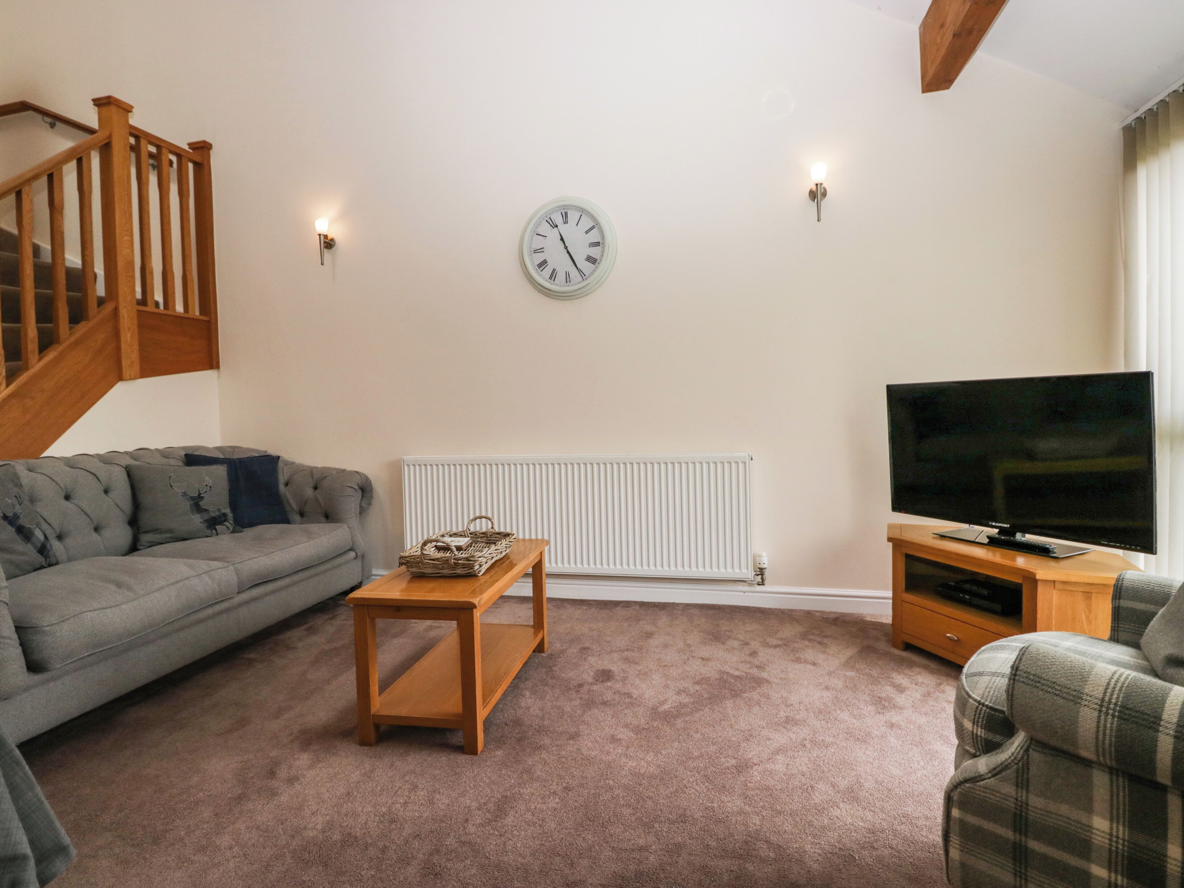 A living room with a grey sofa, a wooden coffee table, a television on a wooden stand, and a white radiator.
