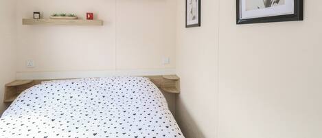 A bedroom with a bed, two wooden shelves, a small plant, and two framed pictures on the wall.