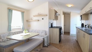 Cucina compatta per camper con angolo pranzo, mobili in legno e piano cottura integrato.