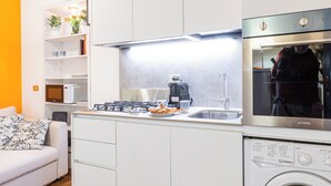 A compact kitchen with white cabinets, a built-in oven, a washing machine, and a wooden ceiling.