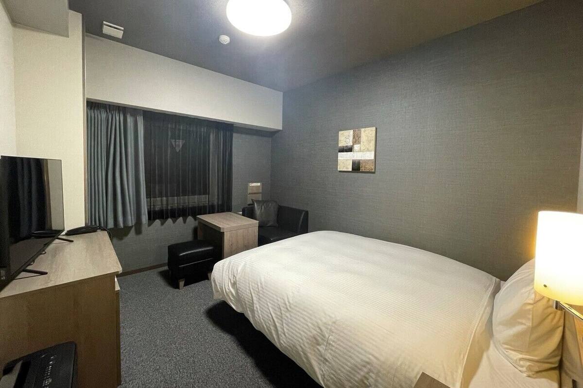Une chambre d’hôtel équipée d’un lit, d’un bureau avec un ordinateur, d’une chaise, d’une télévision et d’une lampe.