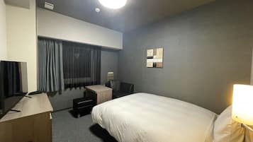 A hotel room with a bed, a desk with a computer, a chair, a TV, and a lamp.