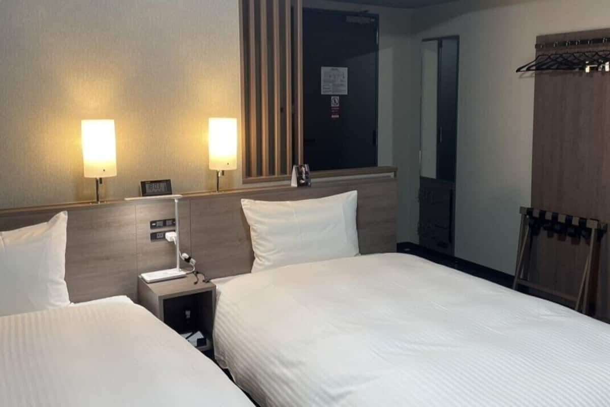 Une chambre d’hôtel avec deux lits, des lampes de chevet, une table de chevet, un miroir et une armoire.