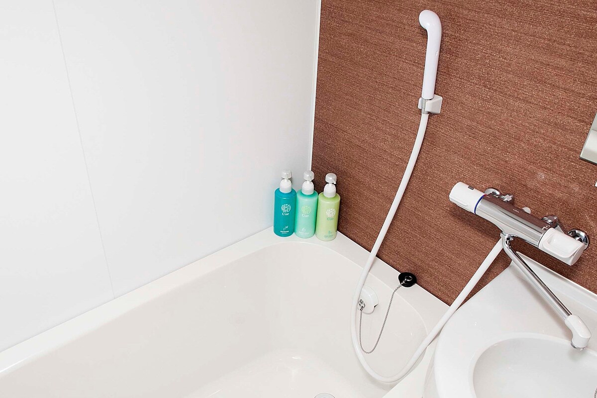 Une salle de bain avec une baignoire, une douche et des toilettes. Trois bouteilles de savon liquide sont posées sur le sol, à côté de la baignoire.