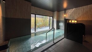 Una piscina interior moderna con una barrera de cristal, paredes de paneles de madera y vistas a un jardín exterior.