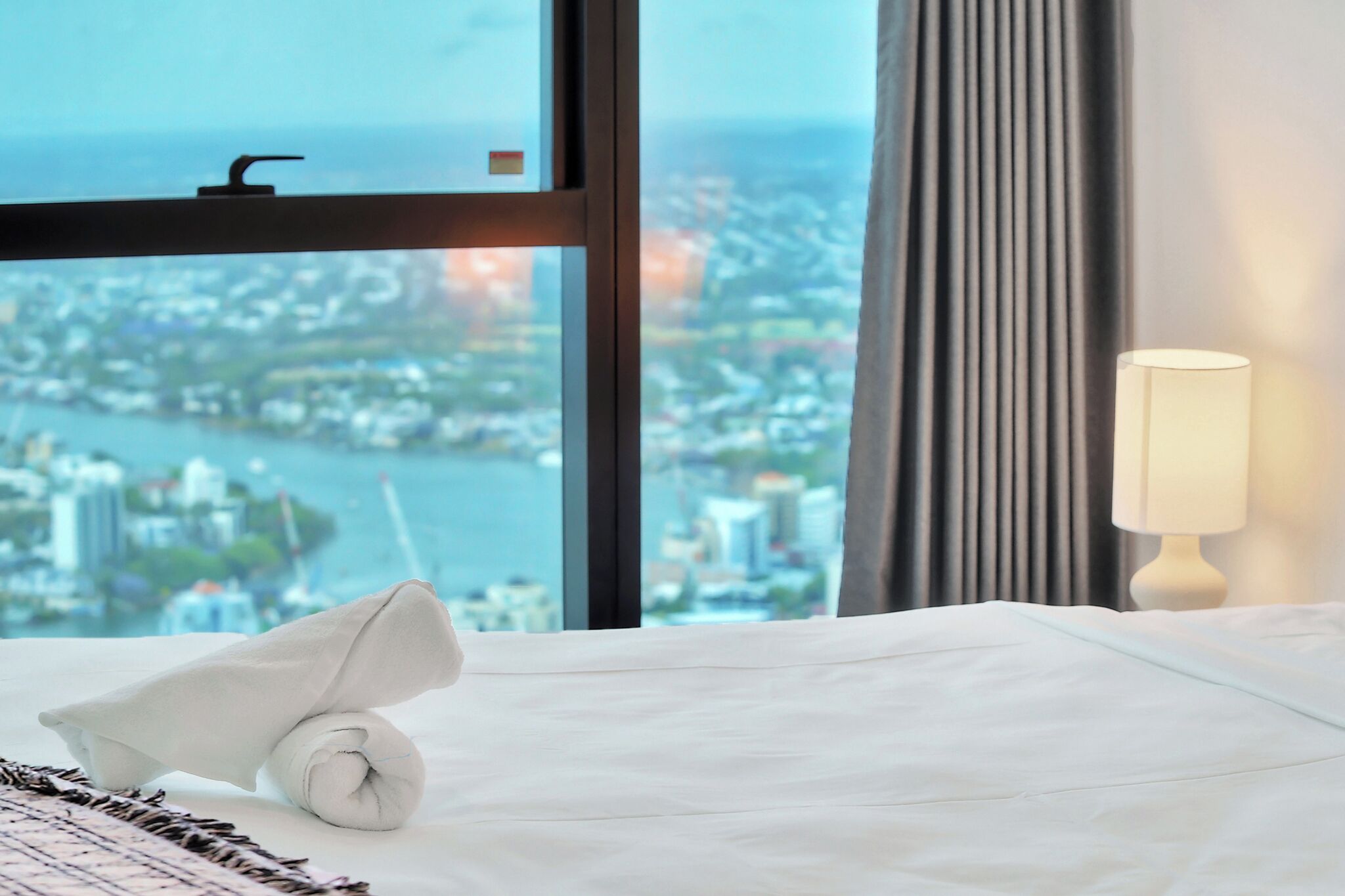 A hotel room with a bed, a window with a city view, and a lamp.