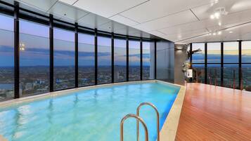 A rooftop infinity pool with a city view, large windows, and a wooden deck.