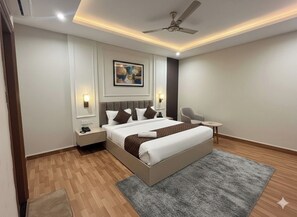 Quarto moderno com uma cama grande, mesas de cabeceira, uma cadeira, ventilador de teto e um quadro na parede.