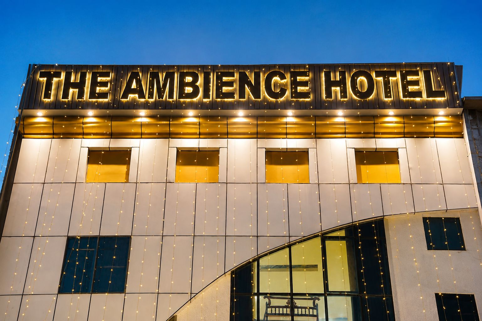 A hotel facade with 'THE AMBIENCE HOTEL' signage, large windows, and a modern architectural design.
