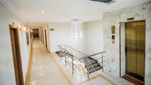 Un pasillo de hotel con una pared de mármol, un ascensor y una escalera con barandillas de metal.