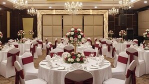 Un salón de banquetes con mesas redondas, manteles blancos y cintas rojas en las sillas.