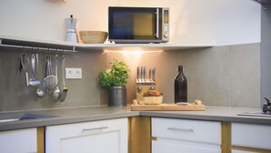 A modern kitchen with white cabinets, a microwave, hanging utensils, a plant, and a cutting board with bread. - Venez Chez Vous Appartement Aux Premières Loges (Sévrier)