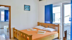 A single-bed room with a wooden headboard, a window with blue curtains, a small bedside table, and a picture on the wall. - Apartment in Croatia near Adriatic Coast (Senj)