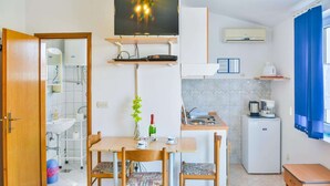 Una cocina compacta con comedor, un televisor sobre la encimera y un refrigerador pequeño.