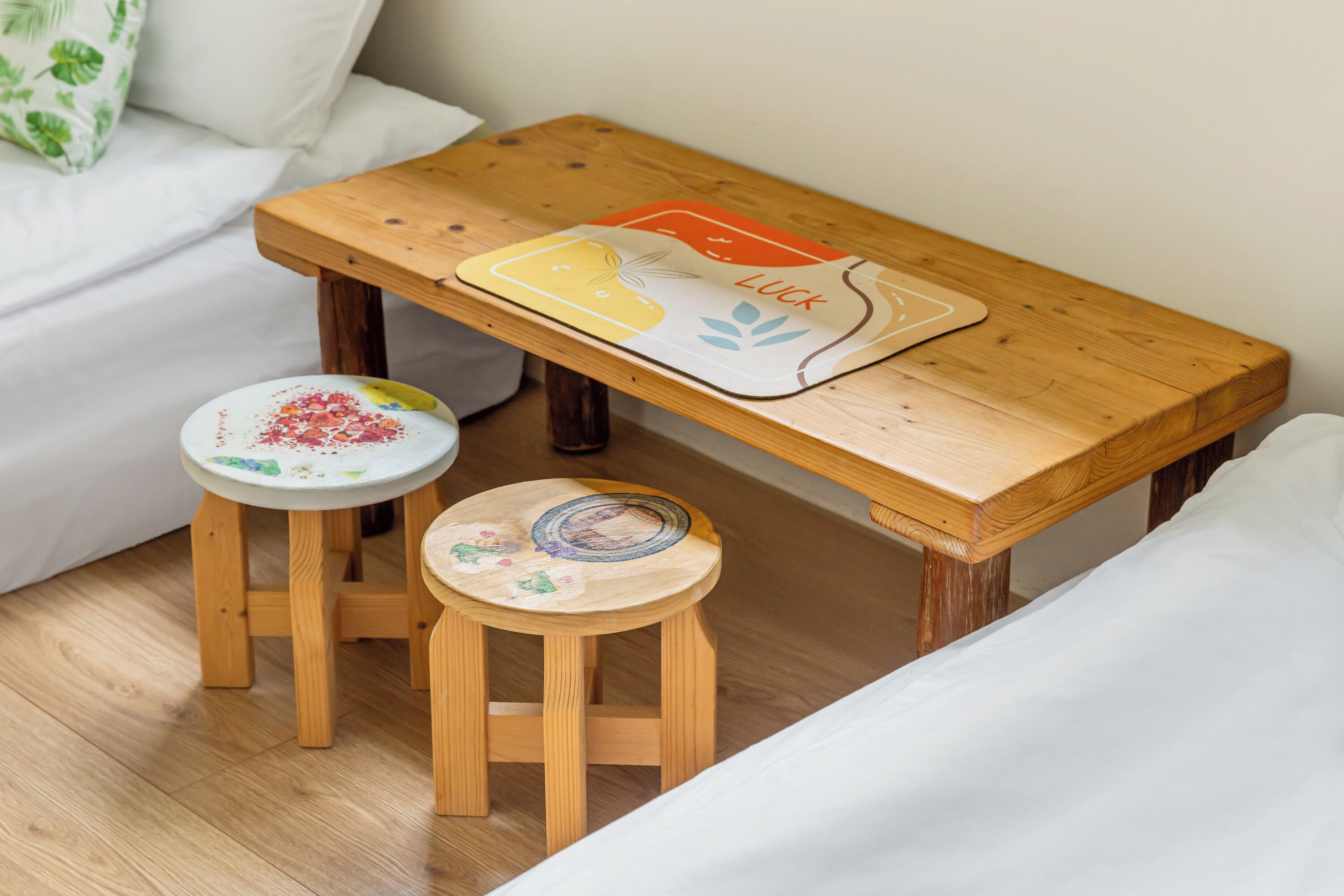 A wooden table with a placemat, two wooden stools, and a white sofa in a room.