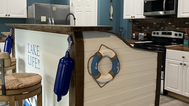 Una cocina con armarios blancos, electrodomésticos de acero inoxidable y una barra con un cartel que dice 'Welcome Onboard'.