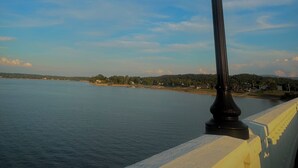 Vista costera con un farol sobre una baranda blanca, con vista a aguas tranquilas y una costa distante.