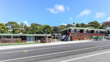 A two-story building with a green roof and a flag on top. There is a parking lot in front of the building.