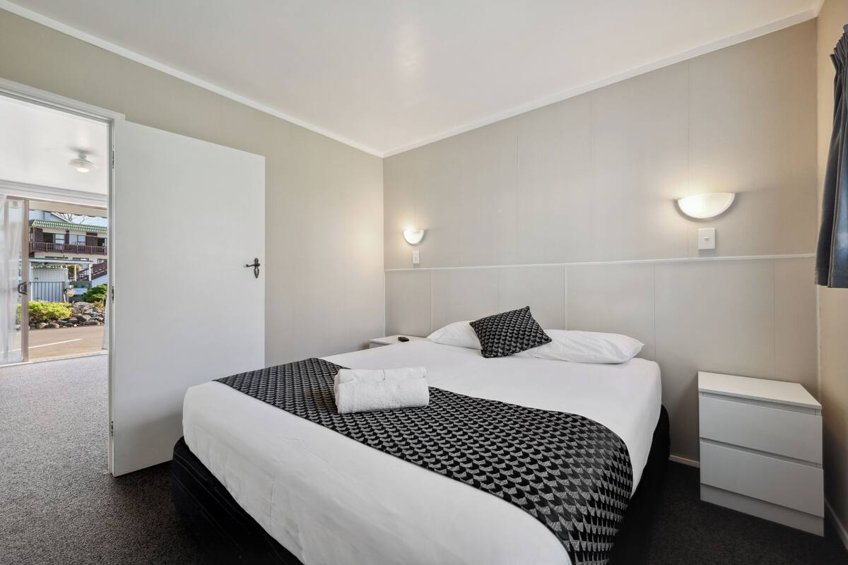 A hotel room with a bed, bedside tables, and a view of the outside.