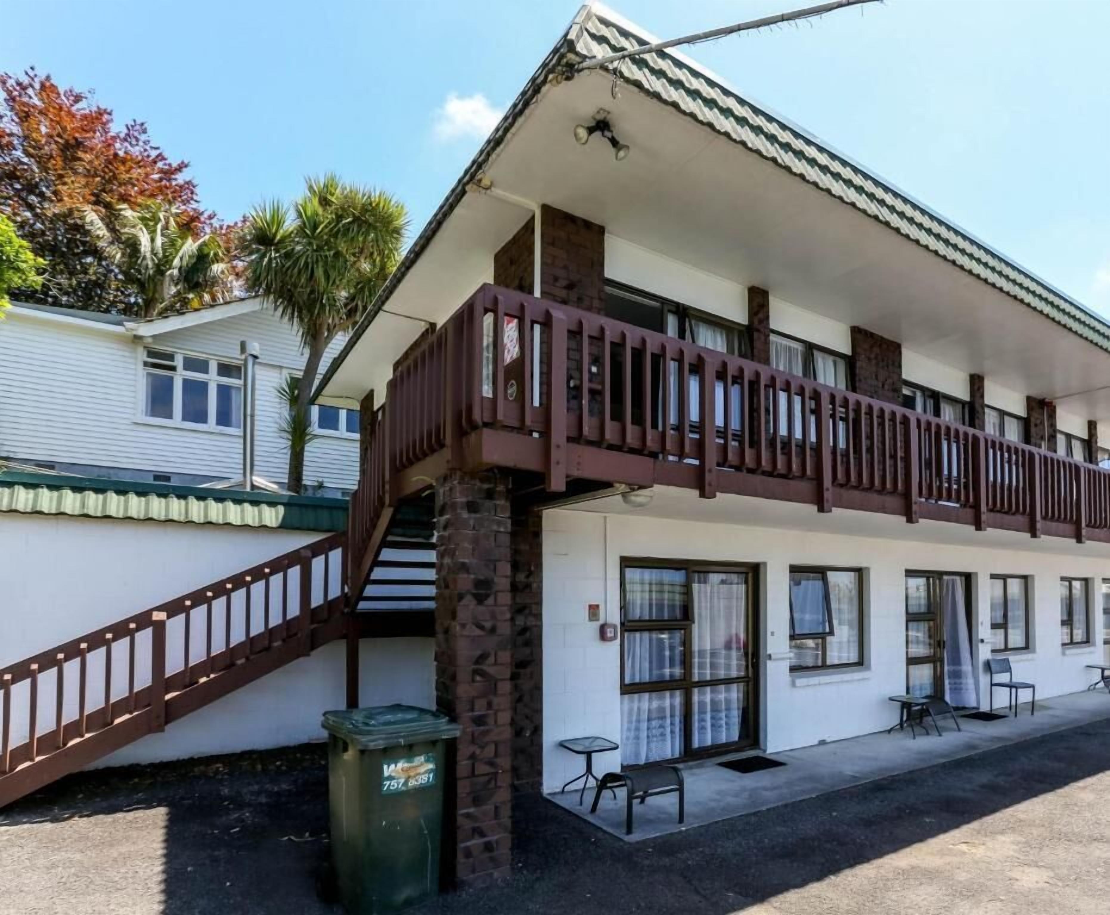 Ein zweistöckiges Motel mit Balkon, Mülleimer und einer kleinen Außenbereich-Sitzgelegenheit.