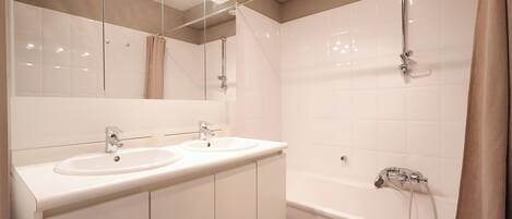 A modern bathroom with two sinks, a large mirror, and a bathtub with a showerhead.