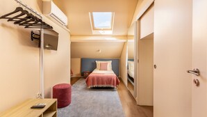 A bedroom with a skylight, a bed, a bedside table, a red ottoman, and a clothing rack. - Central Porto Stay with Balcony (Oporto)