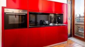A modern kitchen with red cabinetry, a built-in oven, and a coffee machine.
