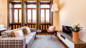 A living room with a sofa, TV, and a large window with a view of buildings.