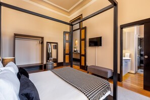 A modern hotel room with a large bed, a bench, a TV, and a bathroom visible through an open door. - Spacious Modern Apartment in Porto (Oporto)