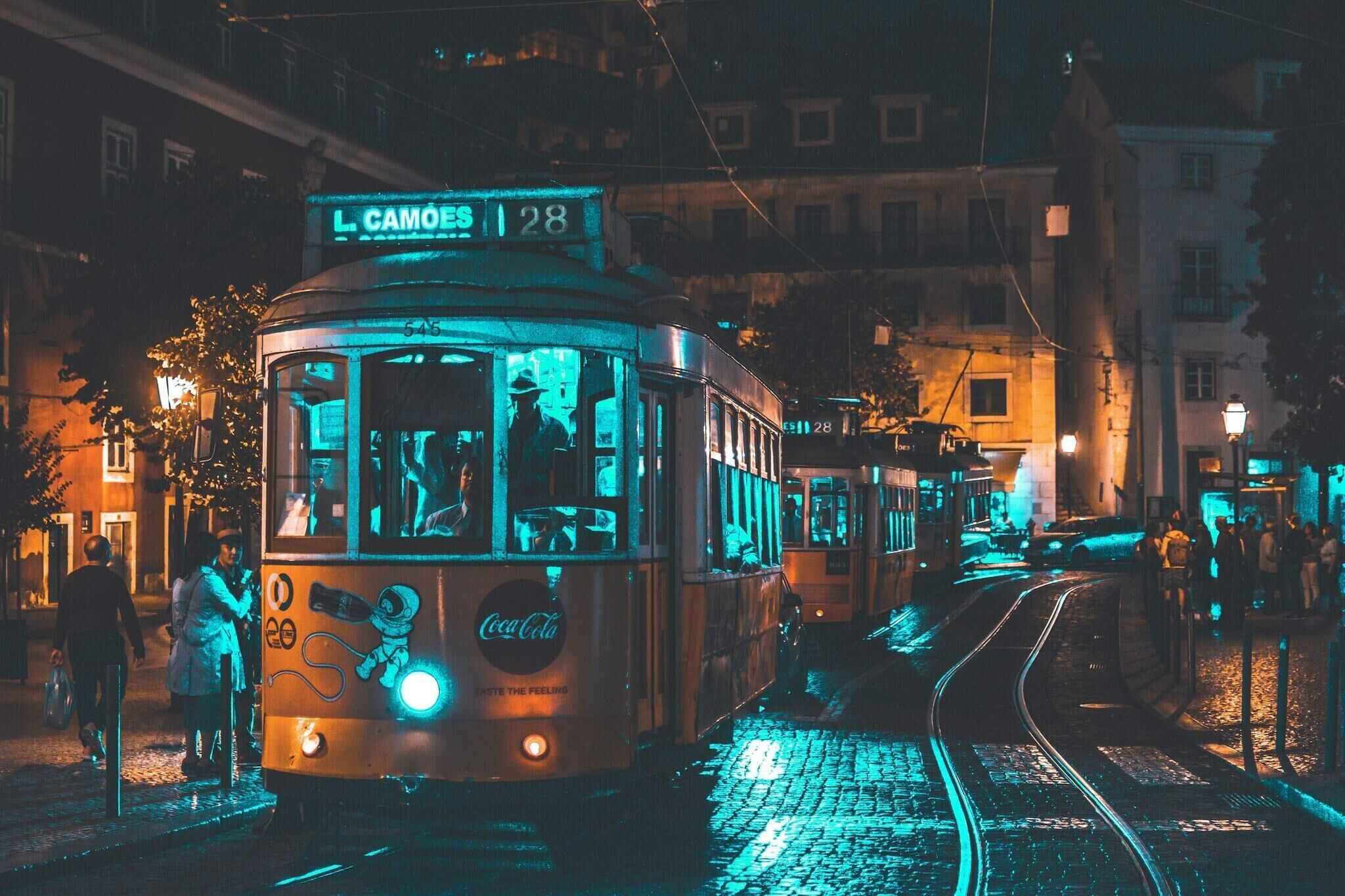 A tram with a visible route number and destination sign, passengers inside, and a tram station platform with people waiting.
