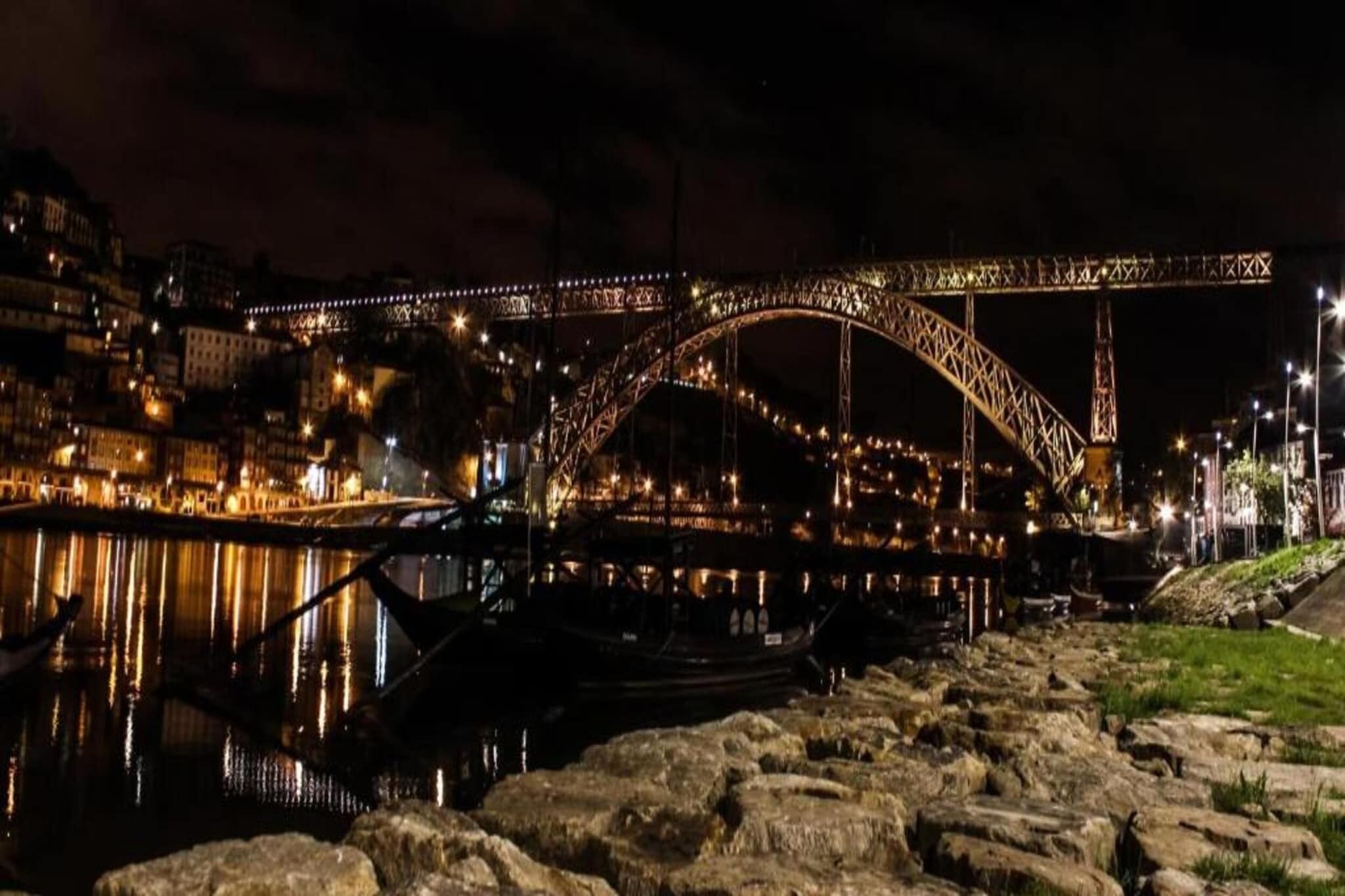 Une vue nocturne d’un pont illuminé, d’une rivière et de bateaux.