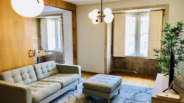 A modern living room with a sofa, ottoman, and a hanging light fixture. - Cozy City Family Retreat (Oporto)