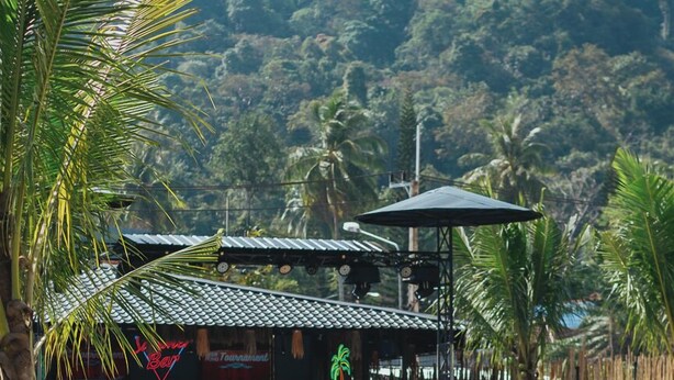 A pool area with people relaxing, a bar with a neon sign, and a tropical backdrop. - Summer Club and Hostel Ao Nang (Krabi)