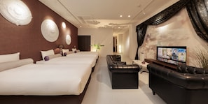 A hotel room with three beds, a black leather sofa, a TV, and decorative wall art.