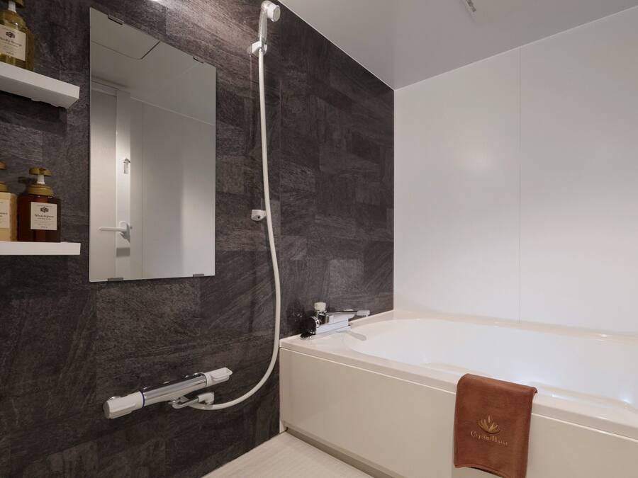A modern bathroom with a bathtub, a shower, and a mirror. There are two bottles of shampoo and conditioner on a shelf.