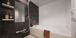 A modern bathroom with a bathtub, a shower, and a mirror. There are two bottles of shampoo and conditioner on a shelf.