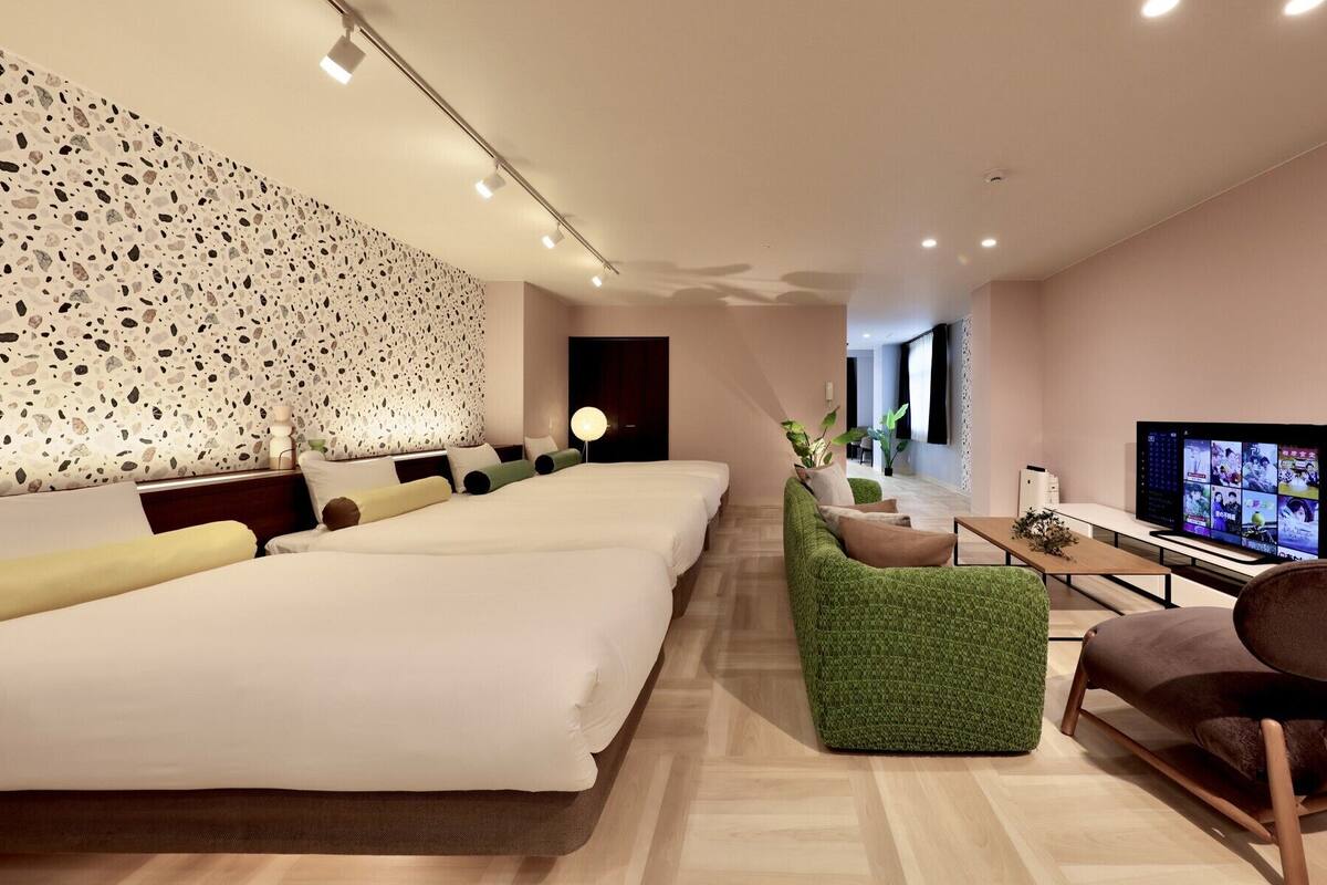 Une chambre d’hôtel avec un grand lit, une télévision, un fauteuil vert et une chaise en bois.