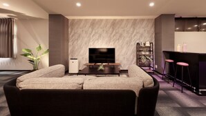 Ein modernes Wohnzimmer mit Sofa, Flachbildfernseher, Couchtisch, einer Pflanze und einer Bar mit Hockern.